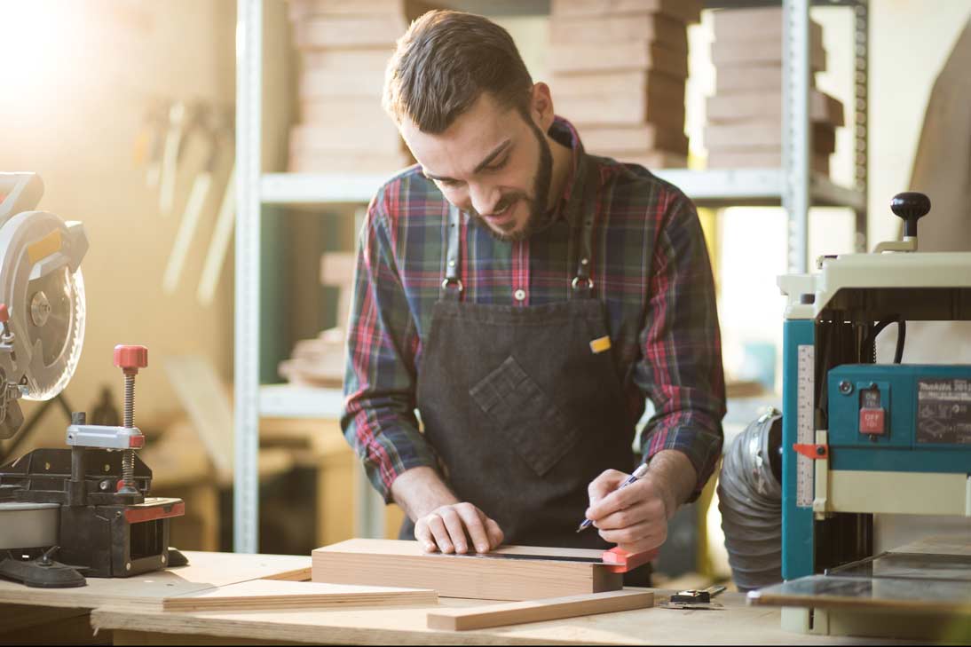 Joven emprendedor trabaja con madera en taller, reflejando esfuerzo y dedicación en su proyecto.