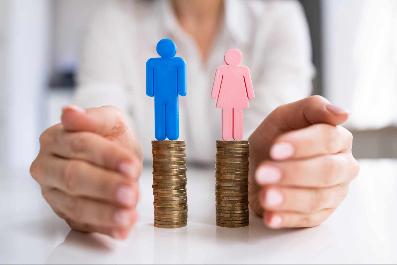 Concepto de brecha de género con figuras masculina y femenina sobre pilas de monedas, representando desigualdad salarial.